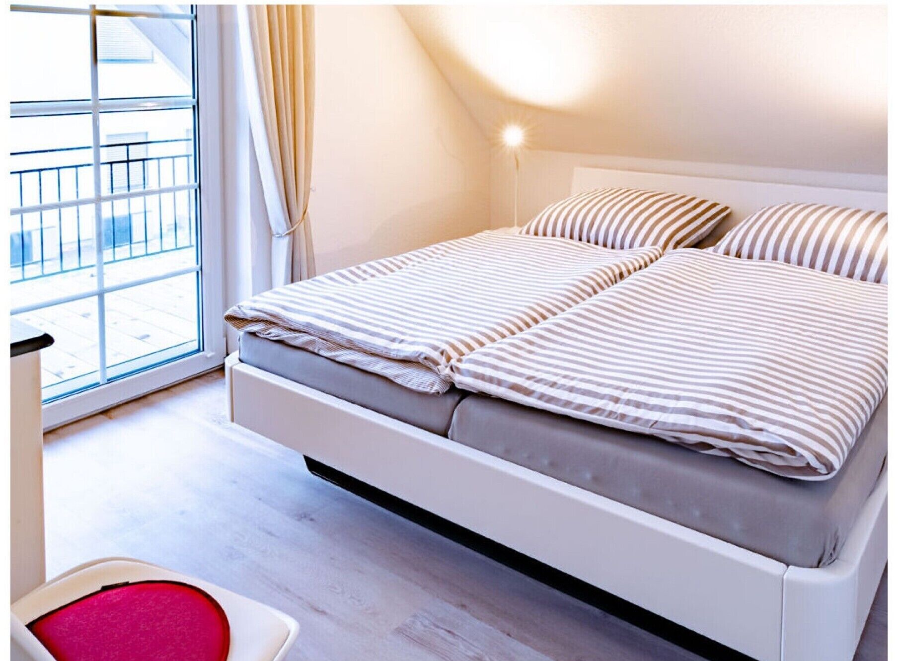 A bed with striped bedding, a bedside table, and a window with curtains.