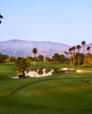 A golf course with a water hazard, palm trees, and mountains in the background. - Coachella 2025-Desert Oasis Resort (Cathedral City)