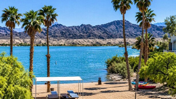 A beach with a pool, palm trees, and mountains in the background. - Island Getaway• Patio View• Boat Ramp & Slips • Pets (Lake Havasu City)