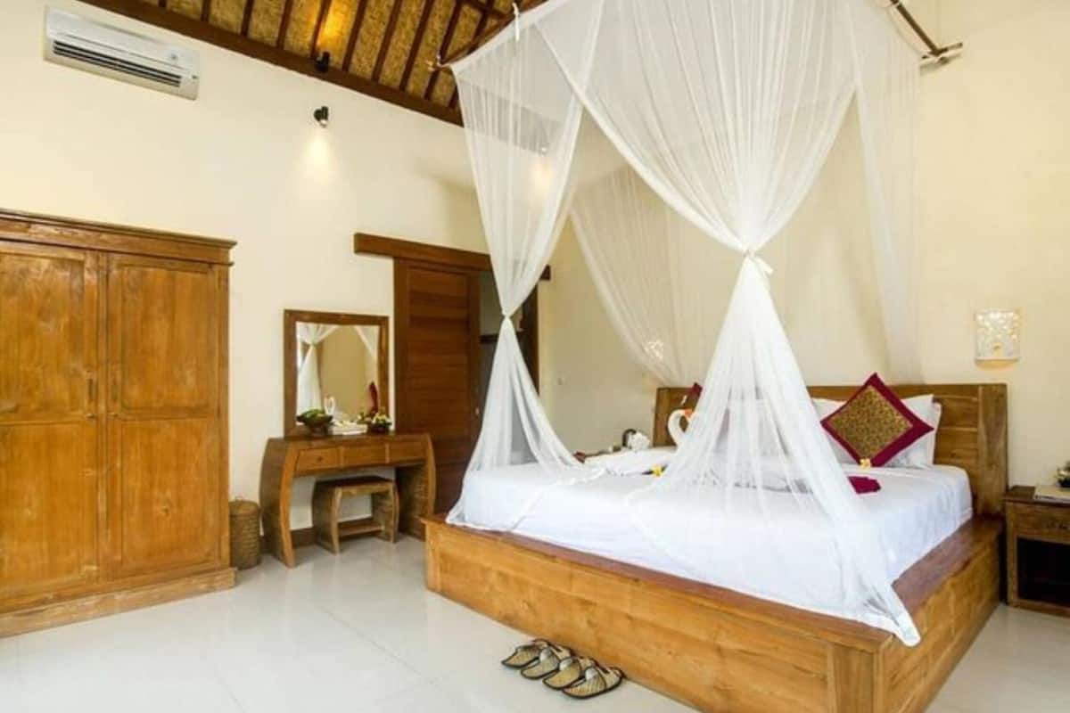 A bedroom with a wooden bed, white canopy, wooden wardrobe, and a small bedside table.