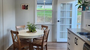 Ein Essbereich mit einem runden Tisch, Holzstühlen, einem Deckenventilator und einem Fenster mit Blick ins Freie.