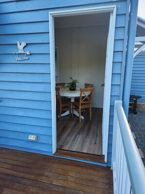 A blue building with a 'Welcome' sign, a wooden deck, and a table with chairs inside.