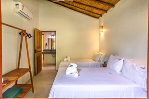 A hotel room with a wooden ceiling, a bed with white bedding, a wooden shelf, and a wall-mounted air conditioner. - Pousada Carmelitha  (Porto Seguro)