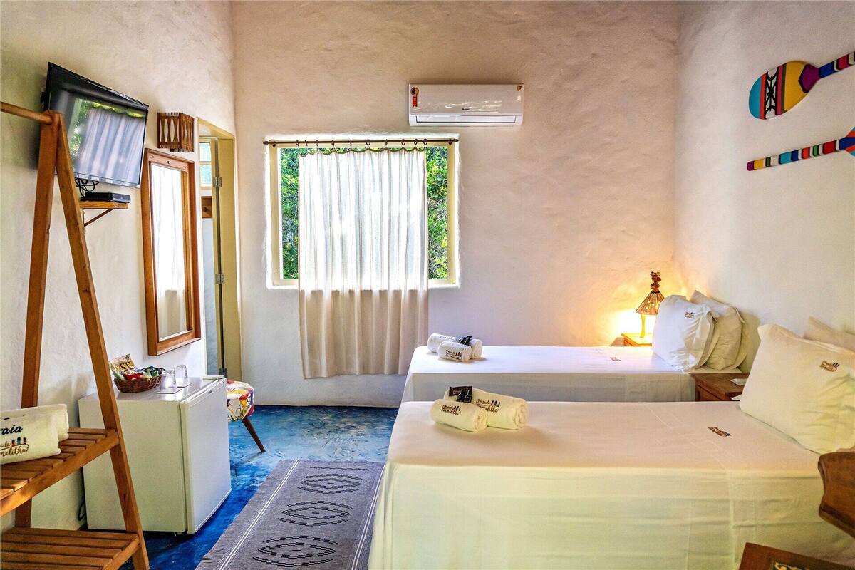 Quarto com cama, uma mesinha com abajur, janela com cortinas, ar condicionado e escada de madeira.