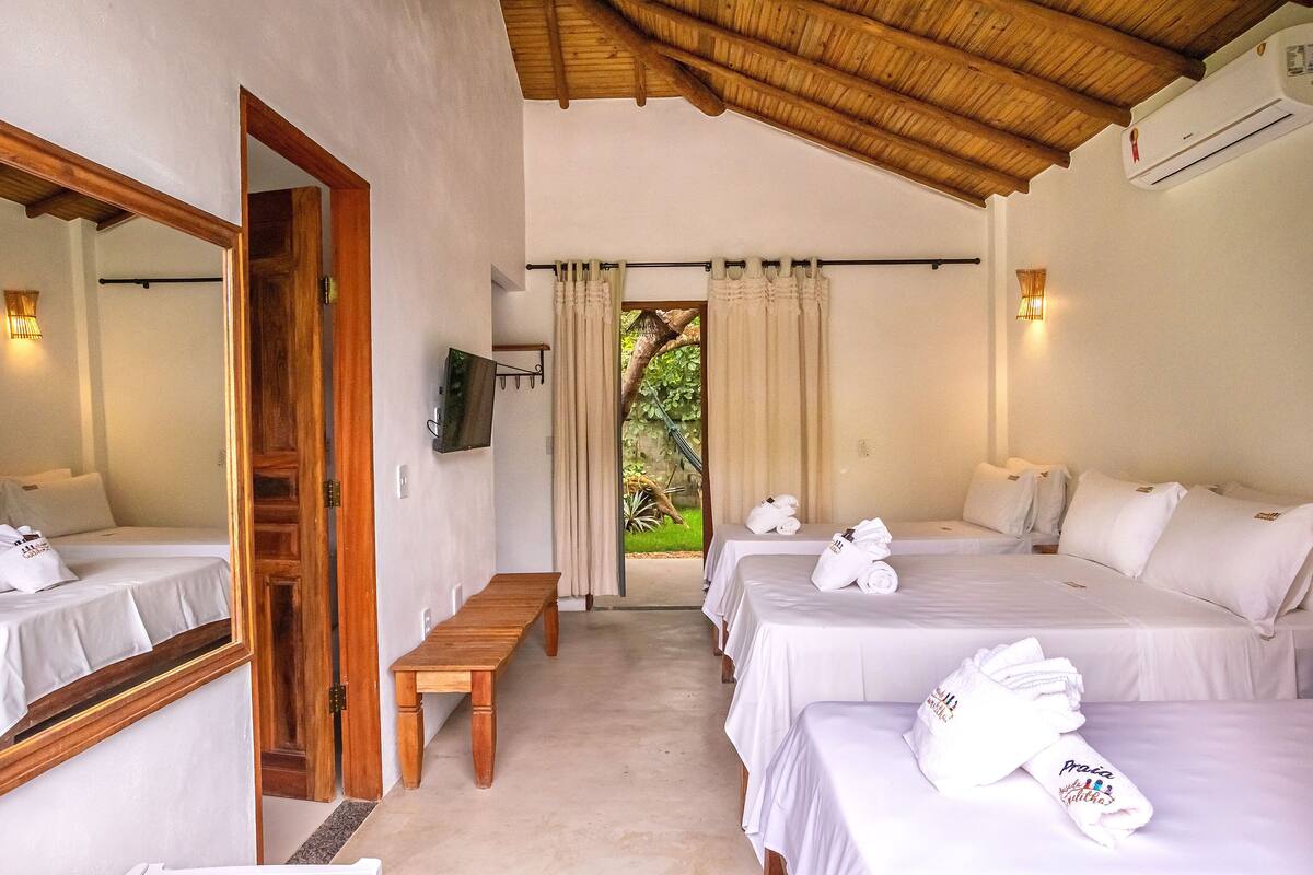 Quarto de hotel com teto de madeira, televisão, um banco e vista para o verde pela janela.