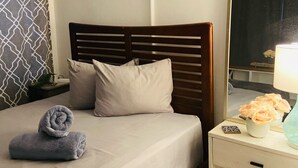 Een netjes opgemaakt bed met een houten hoofdbord, een nachtkastje met een lamp en een spiegel die de kamer weerspiegelt.