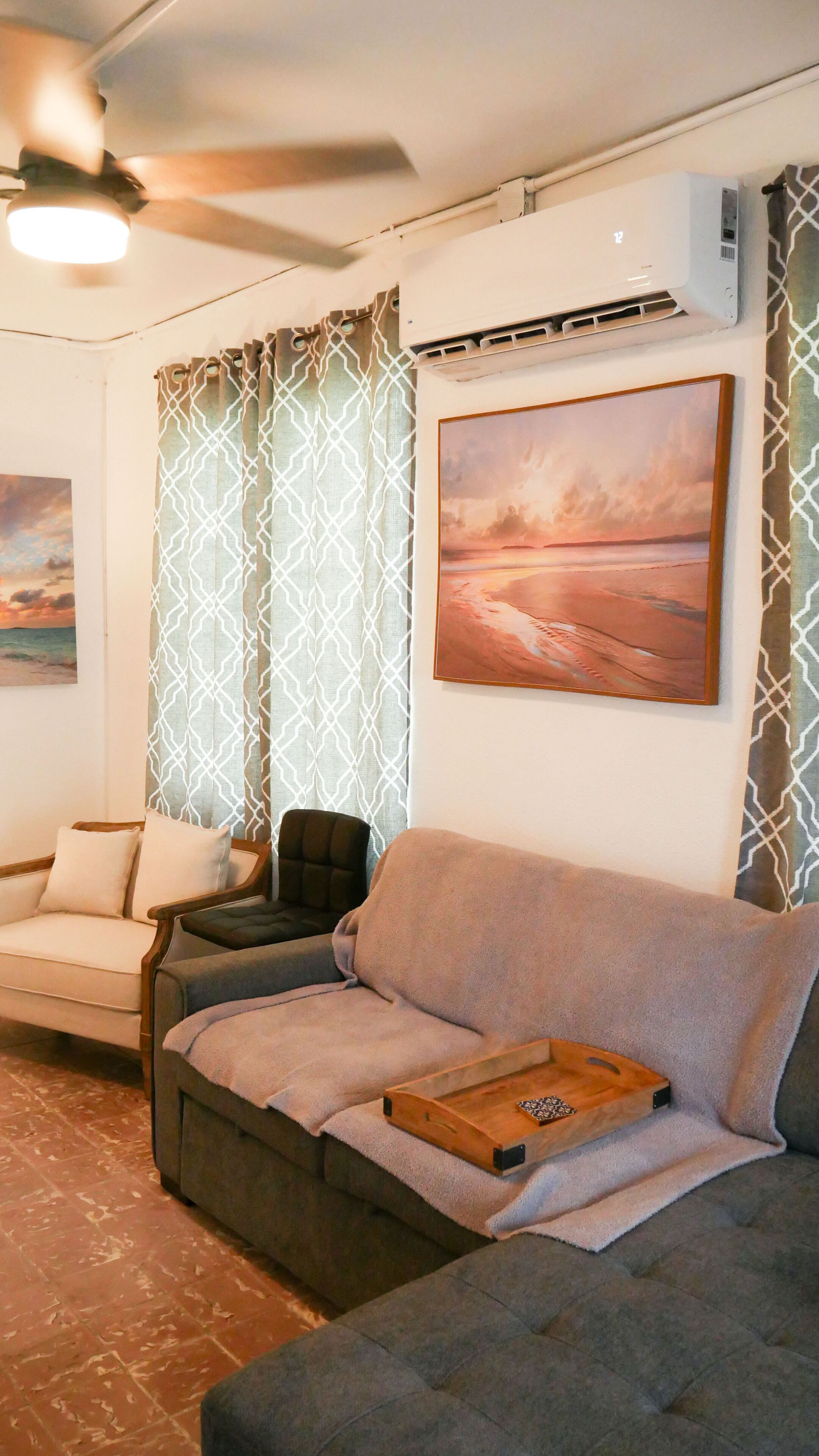 A living room with a grey sofa, a smaller armchair, a wooden tray, and a ceiling fan.