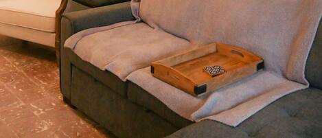 A living room with a grey sofa, a smaller armchair, a wooden tray, and a ceiling fan.