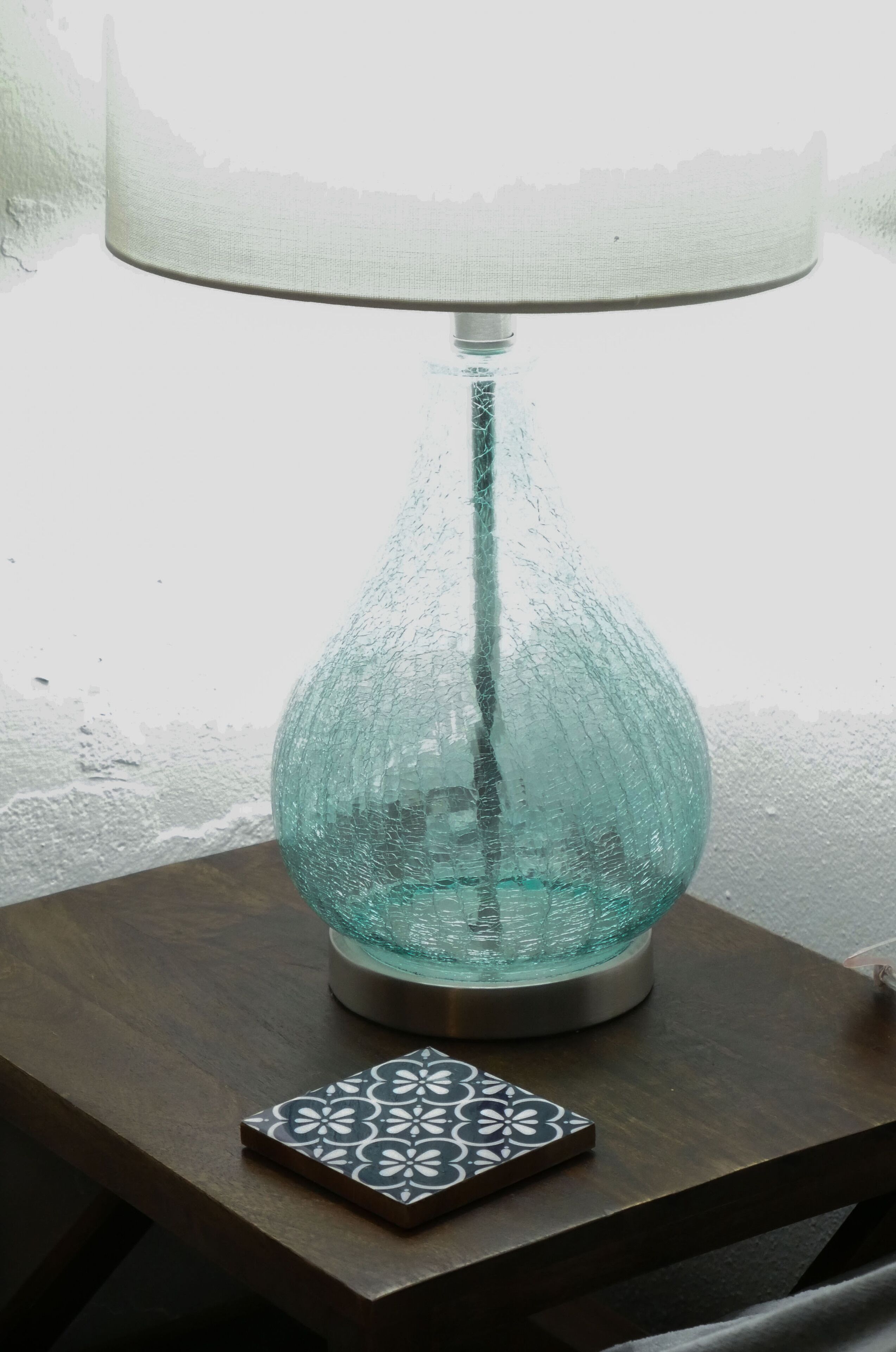 A teal glass table lamp with a white shade on a wooden table.