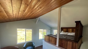 A loft bedroom with a sloped ceiling, wooden beams, a bunk bed, and large windows offering views of greenery. - Entire Place & King Sized Bed (Mountain View)