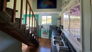 A kitchen with a wooden staircase, a painting above the sink, and a view of the outdoors through a window. - Entire Place & King Sized Bed (Mountain View)