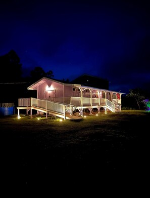 Una casa de dos pisos con porche y terraza cubierta, iluminada durante la noche.