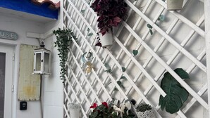 Pared blanca con celosía, varias plantas en macetas, una cesta de mimbre con toallas y una pequeña mesa.