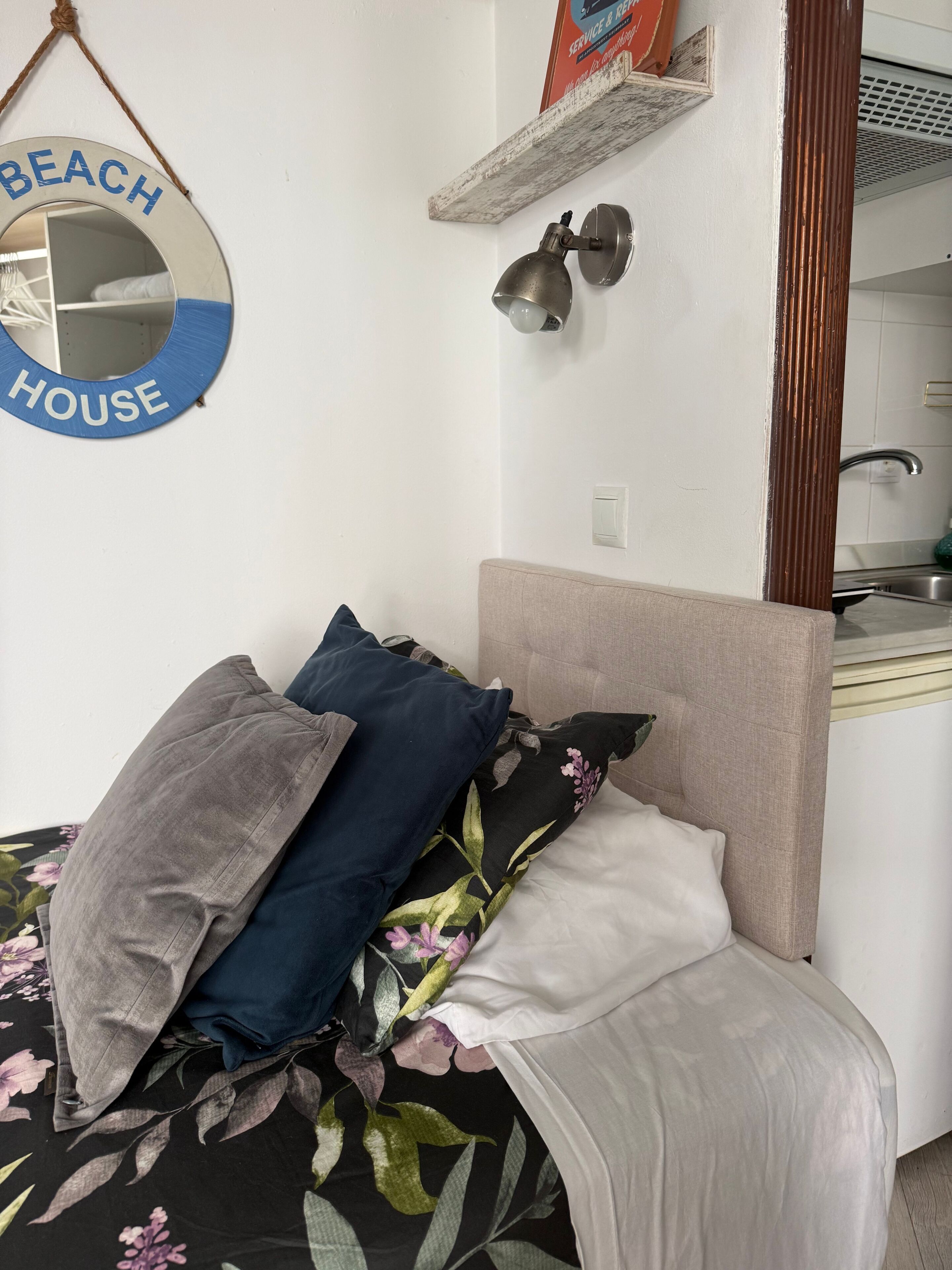 Un lit avec une literie à motifs floraux, une tête de lit et un miroir fixé au mur, sur lequel est inscrit le mot « MAISON DE PLAGE ».