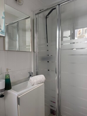 Un baño moderno con cabina de ducha de vidrio, un lavamanos blanco con dispensador de jabón y una toalla.
