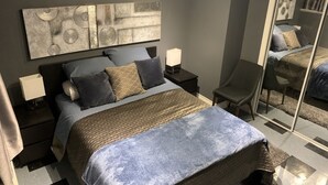 Une chambre à coucher comprenant un lit, des tables de chevet, un miroir et une œuvre d’art murale.