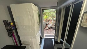 Un espace buanderie comprenant un lave-linge, un sèche-linge, un aspirateur et un tapis noir menant à une porte.