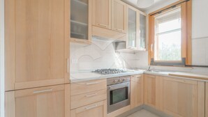 A kitchen with wooden cabinets, a stainless steel oven, and a window with blinds. - Modern Casa Lula with double bathroom, garden and terrace immersed in the greenery of Marina di Camp (Campo nell'Elba)