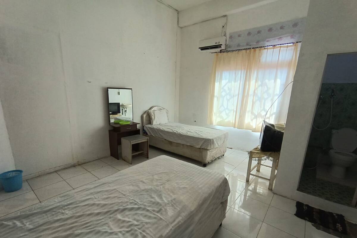 Une chambre avec deux lits, un bureau avec un miroir, un petit tabouret et une fenêtre avec des rideaux.