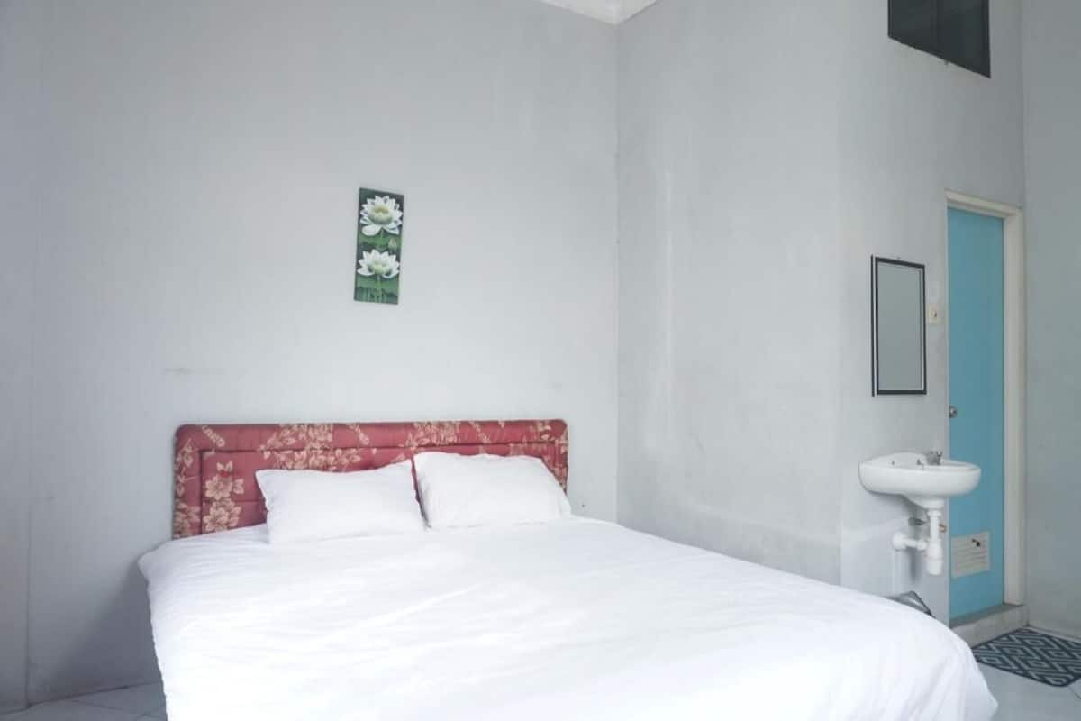 Une chambre avec un lit, un lavabo fixé au mur et une porte.