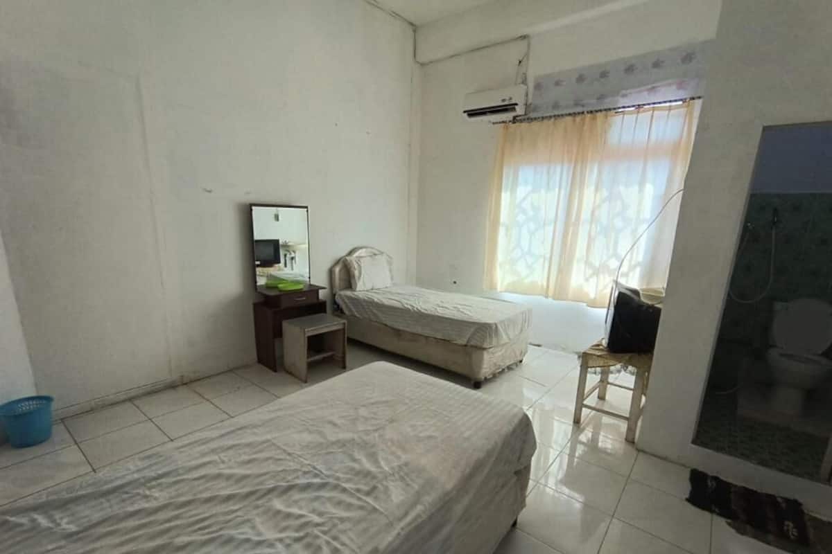 Une chambre avec deux lits, un bureau, une chaise, une fenêtre avec des rideaux et un appareil de climatisation.