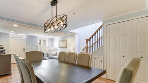 A dining area with a large wooden table, cushioned chairs, and a modern pendant light fixture. - Walk to Main St, City Dock, USNA from Historic Catch 22 w Private Patio (Annapolis)