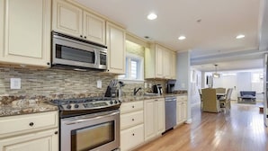 A kitchen with white cabinets, a stainless steel stove, a microwave, and a tiled backsplash. - Walk to Main St, City Dock, USNA from Historic Catch 22 w Private Patio (Annapolis)