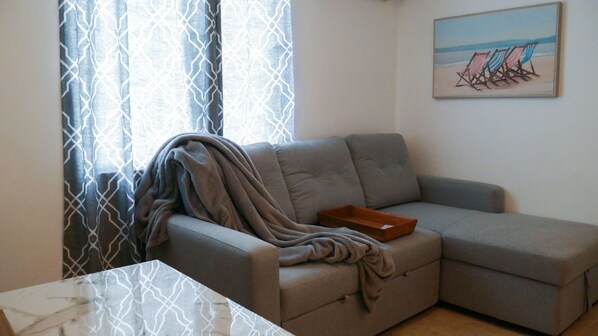 A living room with a grey sofa, a wooden tray, and a painting of beach chairs on the wall.