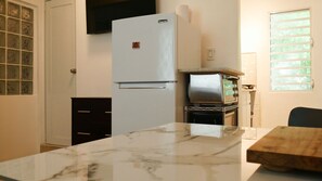 A compact kitchen with a refrigerator, a stove, and a window with blinds.