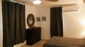 A bedroom with a bed, a dresser, a mirror, and a thermostat on the wall.