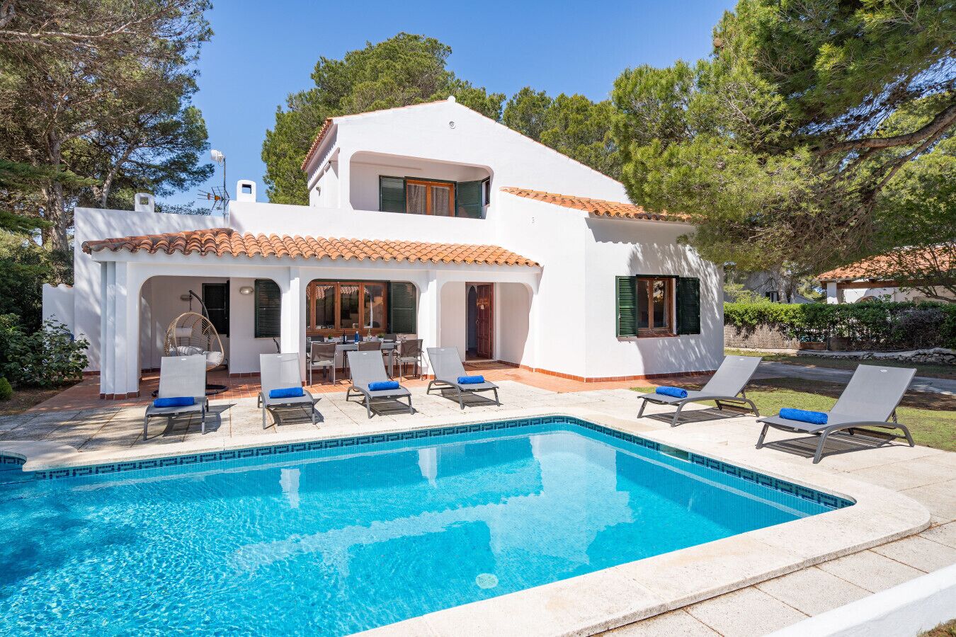 A two-story house with a swimming pool, outdoor seating, and a garden.