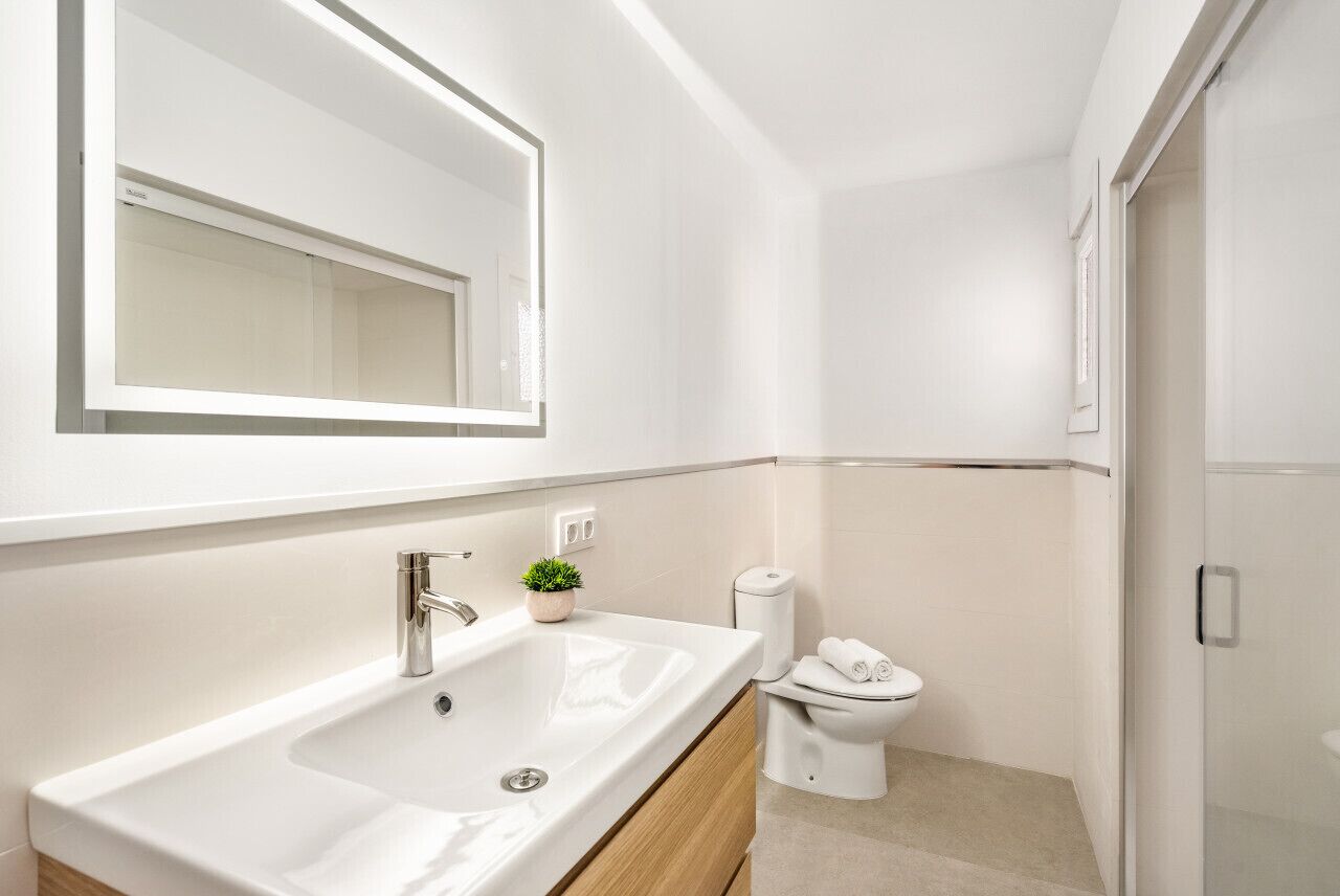 A modern bathroom with a large mirror, a sink, a toilet, and a shower area.