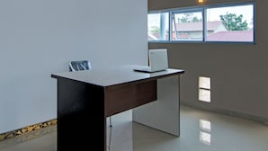 A modern office space with a desk, a laptop, and a window with a view of buildings outside. - Hotel O Putri Homestay Syariah Near SPBU 14.282.694 (Air Hitam) (Pekanbaru)