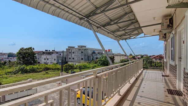 A balcony with a metal roof, a yellow car parked outside, and buildings in the background. - Hotel O Putri Homestay Syariah Near SPBU 14.282.694 (Air Hitam) (Pekanbaru)