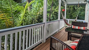 Une terrasse en bois avec des rampes blanches, entourée d’une végétation luxuriante et d’arbres.