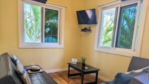 Un salon avec un canapé, une petite table sur laquelle est posée une plante, et un téléviseur fixé au mur.