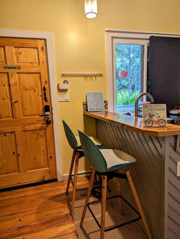 A small kitchen with wooden cabinets, a window with a view of greenery, and a sign that reads "Beach Cottage."