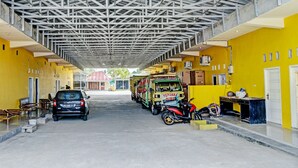 Een overdekte gang met een gele muur, een geparkeerde auto, een motor en een vrachtwagen met een bord.