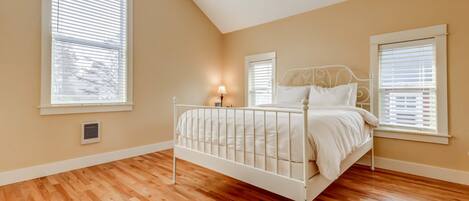 A bedroom with a white metal bed frame, wooden flooring, and two windows with blinds.