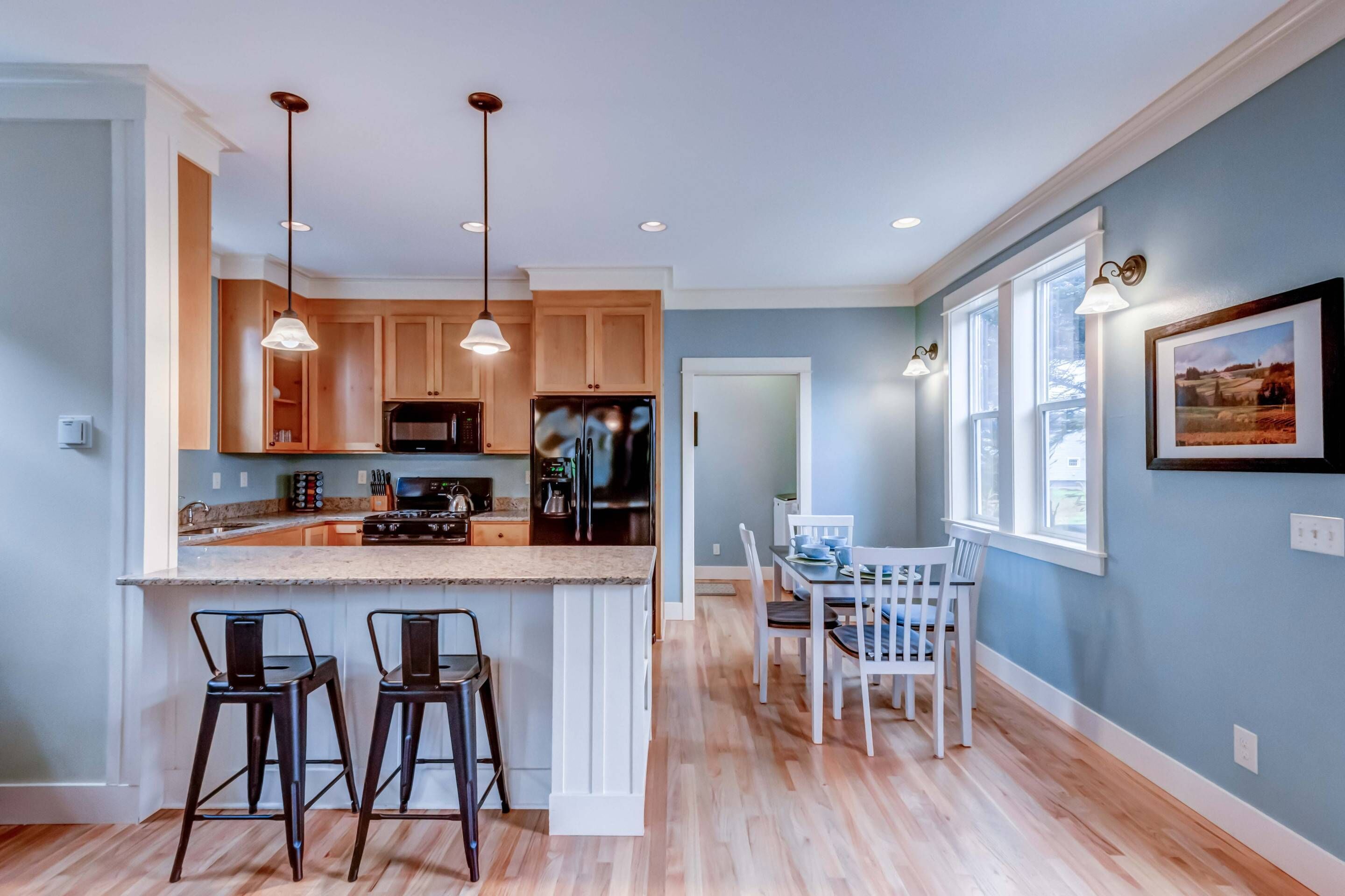 A modern kitchen with wooden cabinets, a central island with stools, and pendant lighting.