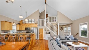 A spacious living area with a dining table, a gray sofa, and a staircase leading to an upper level.