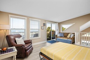 Ein Schlafzimmer mit einem Bett, einem braunen Ledersessel, einem kleinen Tisch mit Lampe und einem Balkon mit einer Couch.