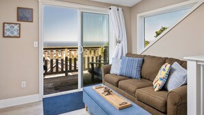 A cozy living room with a brown sofa, a wooden tray, and a view of the sea through a sliding glass door.