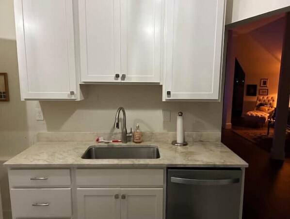 Compact kitchen with cabinetry, sink, and dishwasher, adjacent to a cozy living area with a sofa and small table.