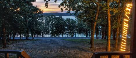 Une vue depuis une terrasse en bois donnant sur un lac, avec des arbres et un coucher de soleil.