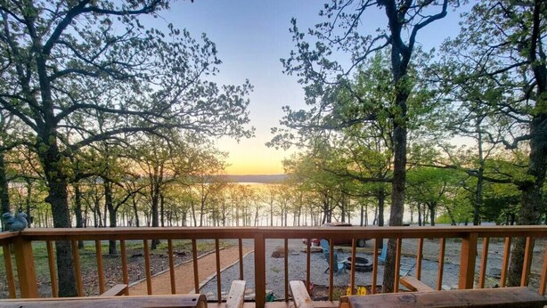 Une terrasse en bois avec des bancs, donnant sur un parking et des arbres.