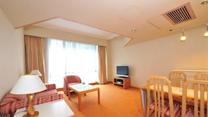 Et hotelværelse med sofa, bord, fjernsyn og et spiseområde med stole.