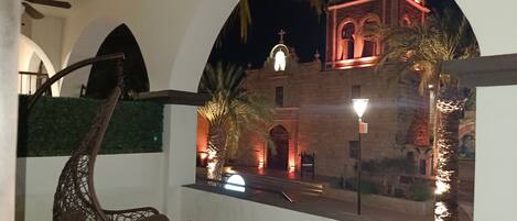 A view of a historic building with a bell tower, palm trees, and a hanging chair.