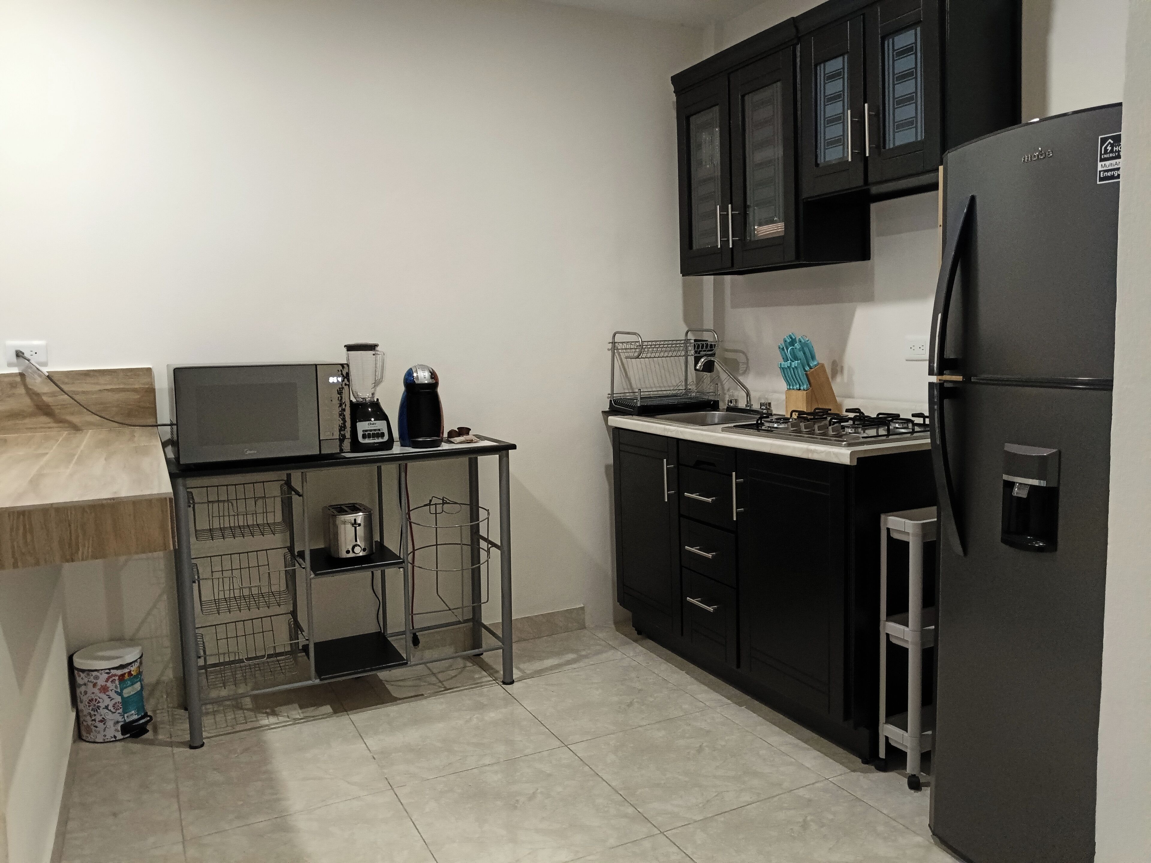 A compact kitchen with a black refrigerator, a coffee maker, a toaster, and a blender on a small table.