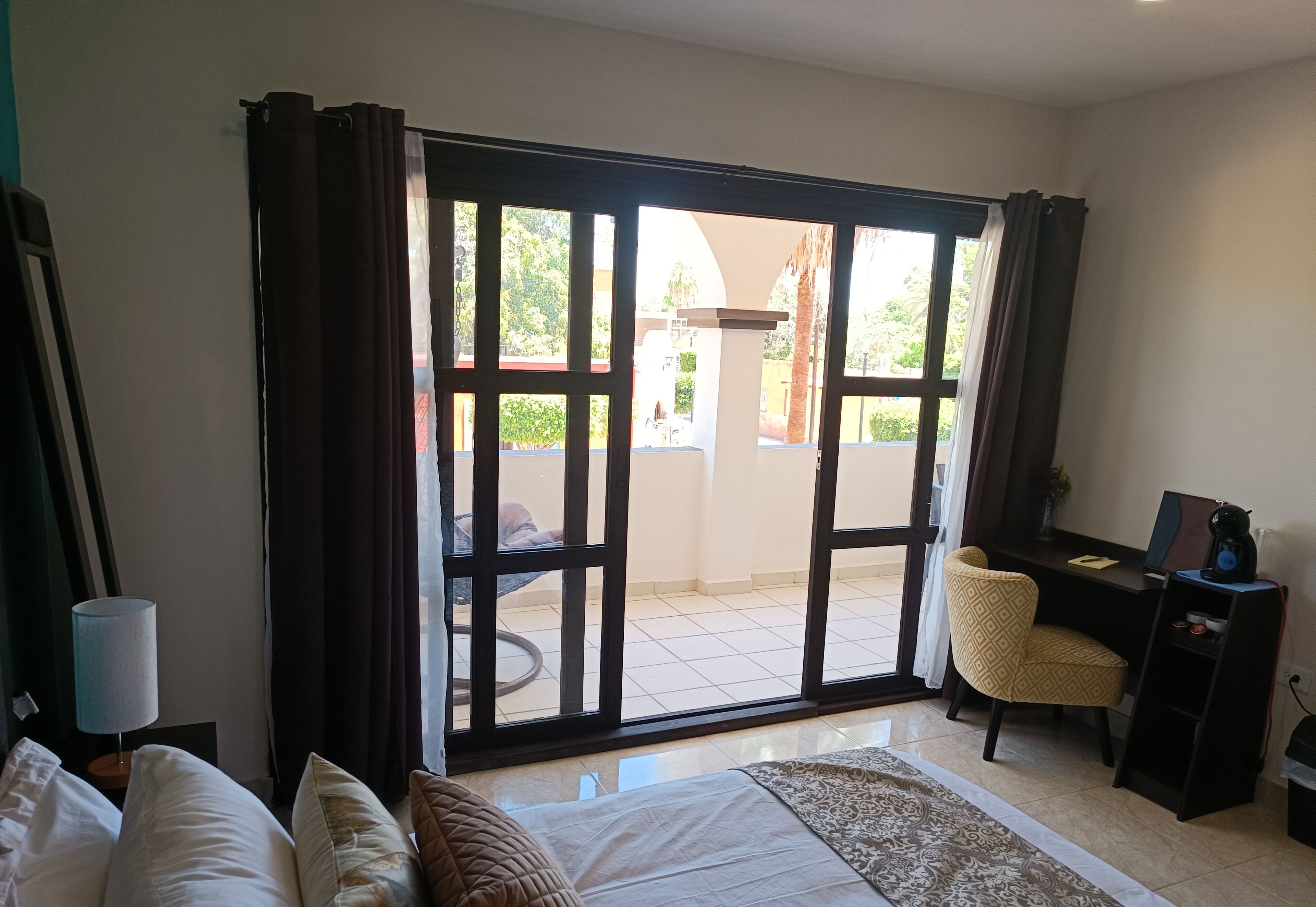 Ein Hotelzimmer mit Bett, Schreibtisch, Stuhl und Blick durch eine Schiebetür auf einen Außenbereich.